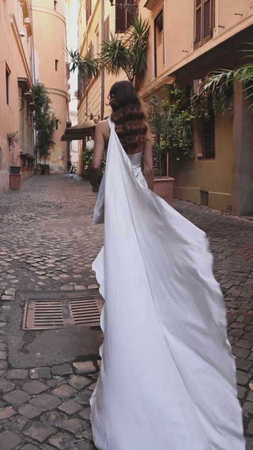 Video: Aetheria mini wedding dress, bride walking away along a cobbled street with the draped train flowing behind